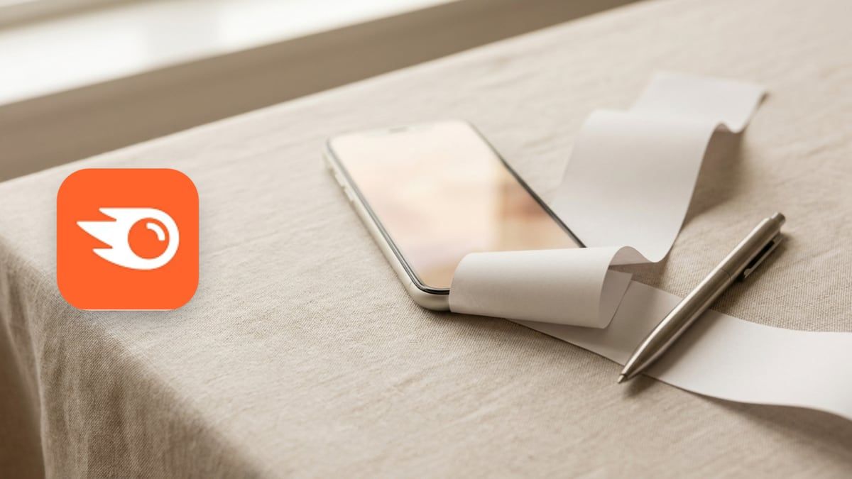 Semrush icon beside a phone and a curling strip of printed paper on a linen surface